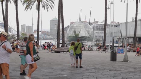 Handheld-clip-of-busy-paved-area-with-groups-of-people-walking-through-shot,-infront-of-Biosfera-glass-sphere-in-Genoa-Port,-Porto-Antico,-in-Italy