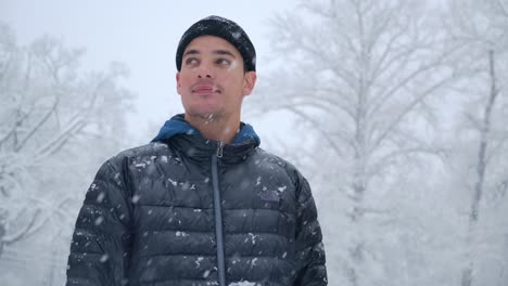 Ein-Mann-Mit-Schwarzer-Kopfbedeckung-Blickt-Auf-Den-Schneefall-Vor-Dem-Hintergrund-Schneebedeckter-Bäume