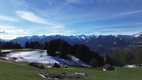 Drone-fly-above-farm-yard-in-the-mountains-and-revealing-amazing-winter-mountain-landscape-with-snow-capped-mountains-on-a-bright-sunny-day