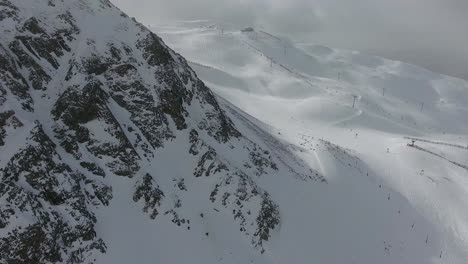 A-4K,-forward-moving-drone-shot-over-backcountry-snowboarders,-hiking-up-the-extreme-terrain-of-the-"East-Wall",-that-looms-over-Arapahoe-Basin-Ski-Resort,-in-the-Rocky-Mountains-of-Colorado