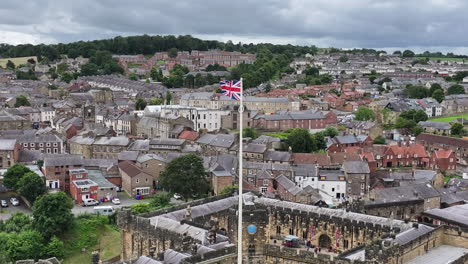 Aerial-View-of-British-Flag-Waving-on-Pole-Above-Alnwick-Medieval-Castle-and-Town,-England-UK