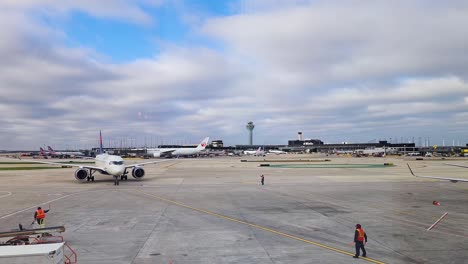 Delta-Airlines-A220,-N119DU,-aircraft-taxis-into-gate-at-O'Hare-international-airport-with-marshallers-visible-and-control-tower-in-the-background