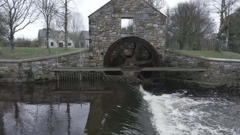 Old-water-mill-with-rotating-wheel-on-a-river,-generating-eco-friendly-energy-in-Ballinode,-Ireland,-cloudy-day