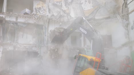 Una-Nube-De-Polvo-Reduce-La-Visibilidad-Mientras-Una-Excavadora-Derriba-Un-Edificio-De-Hormigón.