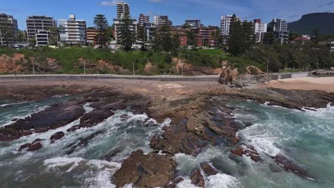 Aerial-reveal-of-rocks-and-surf-and-a-fisherman-preparing-his-gear-on-the-rocks