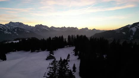 Yellow-orange-sunset-haze-glow-spread-across-horizon-backlit-of-rugged-swiss-mountains-overlooking-lake,-Amden-Weesen-Switzerland