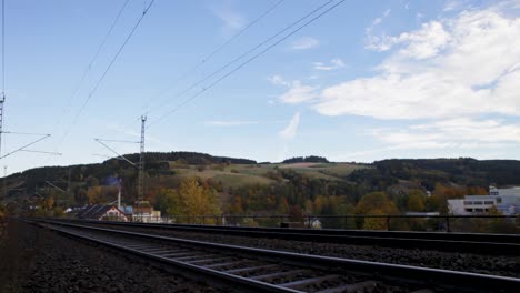 Eisenbahnschienen-Erstrecken-Sich-Bis-Zu-Einem-Horizont,-Gesäumt-Von-Herbstbäumen-Und-Sanften-Hügeln,-Unter-Einem-Weiten-Himmel-Mit-Weichen-Wolken