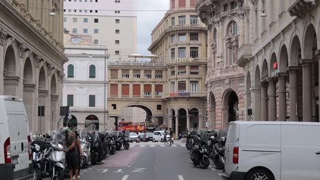 Zeitlupenclip-Mit-Schwenk-Nach-Unten,-Der-Eine-Belebte-Stadtstraße-In-Genua,-Italien,-Mit-Verkehr,-Geparkten-Fahrzeugen-Und-Fußgängern-Zeigt,-Die-Die-Straße-überqueren