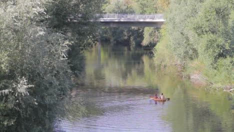 Gente-Navegando-En-Kayak-Bajo-Un-Puente-Sobre-Un-Río-Tranquilo-Rodeado-De-Frondosos-árboles