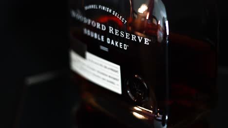 Tomando-Una-Panorámica-De-Una-Botella-De-Whisky-Bourbon-Puro-De-Kentucky-De-Doble-Roble-Woodford-Reserve,-Poca-Profundidad-De-Campo-Con-Fondo-Negro