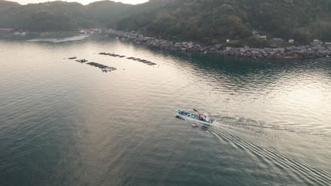 Aerial-Panoramic-Drone-Fly-Above-Japanese-Sea-With-fishing-boat-sailing-boathouses-houses-hills-and-sunshine-through-Kyotango-Kyoto-Japan,-beach-travel-destination-in-Asia