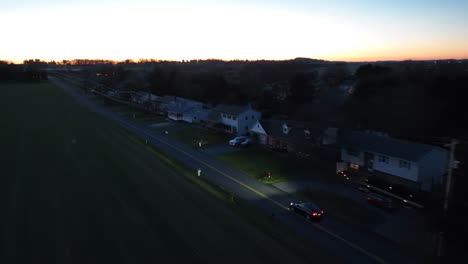 Aerial-tracking-shot-of-Tesla-Model-Y-driving-on-suburban-residential-road-at-sunset