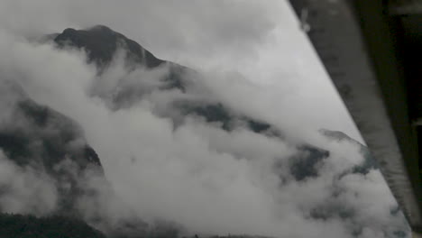 Slow-motion-rain-drops-fall-off-side-of-boat-in-foreground-with-focus-on-cloudy-mountains-behind---Doubtful-Sound-,-New-Zealand