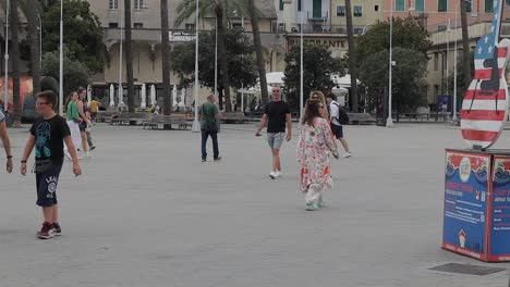 Groups-of-people-walking-through-open-paved-area-with-palm-trees-in-Italy