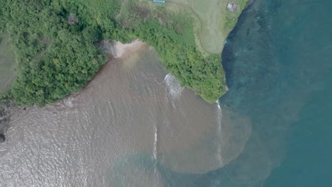 Top-down-aerial-drone-shot-over-polluted-sewage-water-and-floating-trash-with-debris-over-dead-coral-reef-mixing-with-turquoise-water-and-tropical-coastine-in-Bali-Indonesia