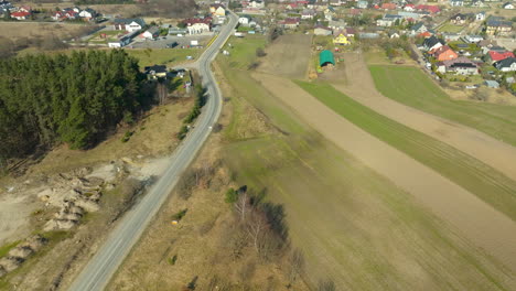 Aerial-view-of-a-road-leading-into-a-rural-village-with-houses-and-fields