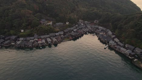 Aerial-bay-sunset-reflected-on-Japan-Sea-Stilt-houses-at-Kyotango-Beach-travel-destination,-traditional-wooden-houses,-establishing-drone-Asian-panoramic-landscape