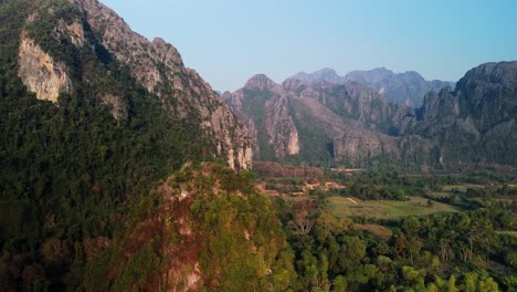 Formaciones-De-Piedra-Caliza-En-El-Campo-Rural,-Con-La-Bandera-De-Laos-En-La-Colina