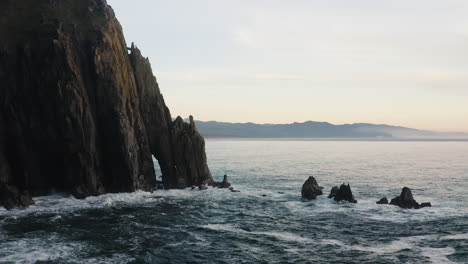 Pacific-Ocean-waves-crashing-against-Oregon-Coast-cliffs,-low-aerial-flyover