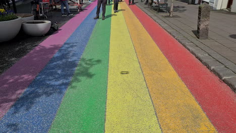 Rainbow-Street-in-Downtown-Reykjavik,-Iceland,-Tourists-Walking-on-Colored-Road-on-Sunny-Day