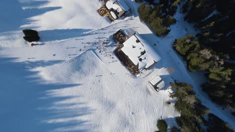 Aerial:-Birds-Eye-View,-Drone-flying-Down-to-a-Ski-Bungalow,-surrounded-by-a-slope-with-skking-people