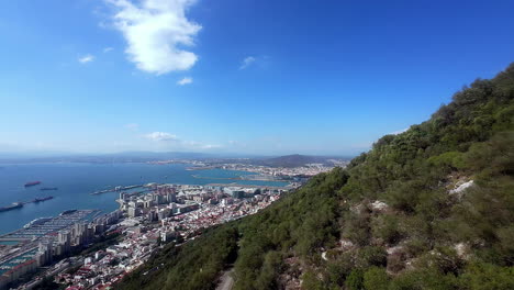 Drones-Aéreos-Vuelan-Sobre-El-Pueblo-Costero-Mediterráneo-En-El-Estrecho-De-Gibraltar,-Horizonte-Azul-Y-Colinas-Verdes,-Estableciendo-Un-Paisaje-Panorámico-De-Playa-Con-Luz-Diurna