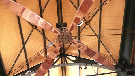 A-huge-wooden-ceiling-fan-operating-with-mechanical-components-rotates-in-a-large-warehouse