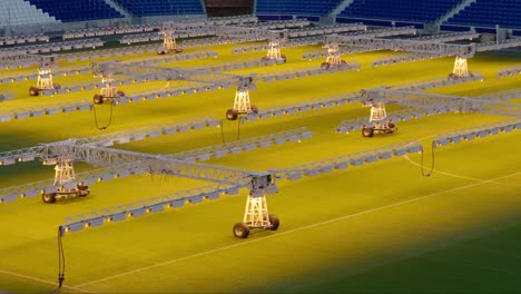 Row-of-grow-lights-on-wheels-illuminating-grass-in-an-empty-football-stadium,-maintenance-concept,-evening-light