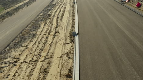 Close-aerial-view-of-a-newly-paved-road-beside-a-dirt-track