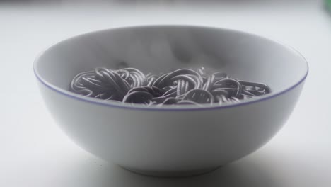 White-bowl-with-hot-black-sepia-noodles-on-white-background