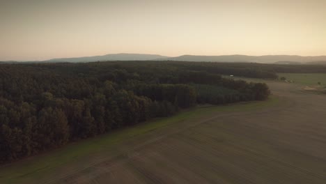 Dramatic-and-epic-drone-shot-of-the-woods-and-fields-with-mountains-in-the-background-bird-view,-during-a-sunset-or-a-sunrise-dusk-or-dawn