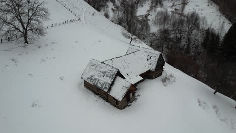 Snow-covered-cabin-in-the-Cindrel-Mountains-during-winter,-aerial-view