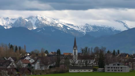 Kirche-Im-Vordergrund-Der-Schneebedeckten-Bergketten-In-Einem-Wohngebiet,-Dorf