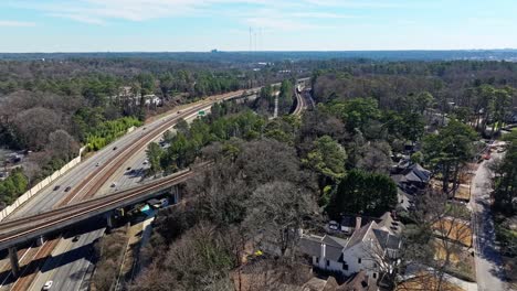 Aerial-flyover-forest-suburb-neighborhood-with-traffic-on-highway-and-rail-tracks