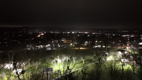 drone-flies-over-green-grass-city-park-in-small-town-at-night-while-cars-drive-by-at-night