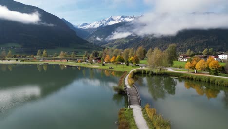 Scenic-Lake,-Footbridge-and-White-Mountain-Peaks-during-Autumn-in-Austria---Aerial-4k