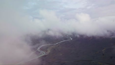 Fliegen-Sie-Durch-Die-Wolken-Hoch-über-Einem-Gletscherflussbett,-Das-Sich-Durch-Die-Isländische-Landschaft-Schlängelt