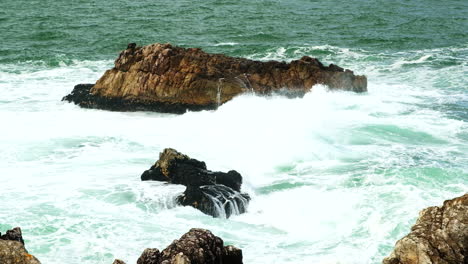 Swell-surges-over-coastal-rocks-of-Hermanus-with-frothing-whitewater,-telephoto