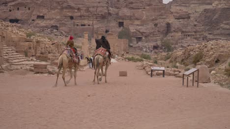 Bedouins-riding-camels-towards-the-Roman-theatre-in-Petra-Jordan,-archeological-site