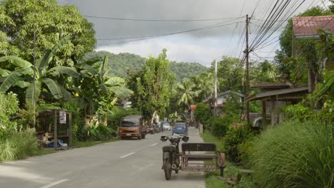 Car-drives-tropical-southeast-asian-Road-in-Philippines-greenery-traditional-houses-and-old-motorcycle,-countryside-feeling