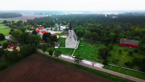 big-gray-church-on-a-green-meadow-in-the-fog,-cemetery,-visby,-sweden,-drone