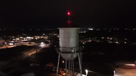 Drone-Volando-En-órbita-Alrededor-De-La-Torre-Del-Tanque-De-Agua-De-Una-Pequeña-Ciudad-Por-La-Noche-Con-Luz-Roja-En-La-Parte-Superior