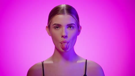 Cheeky-young-woman-sticks-out-tongue,-purple-studio-light,-pink-background