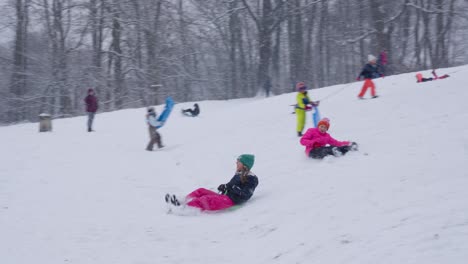 Children-sledging-in-winter-wonderland-while-snowflakes-falling-in-the-park---Woluwe-Saint-Pierre,-Belgium---Slow-motion