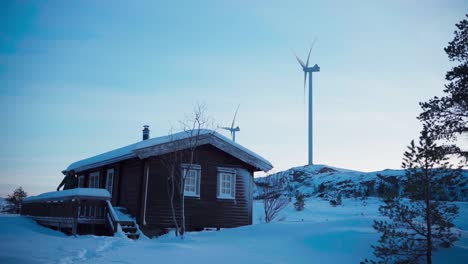 Ein-Mann-Schlendert-Von-Der-Holzhütte-Weg,-Inmitten-Des-Schneebedeckten-Geländes,-Im-Hintergrund-Sind-Windräder-Zu-Sehen,-In-Bessaker,-Provinz-Trondelag,-Norwegen-–-Statische-Aufnahme