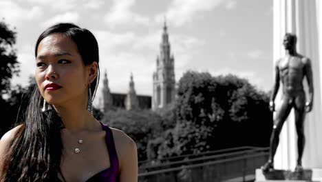 Beautiful-Asian-woman-turning-towards-greek-style-black-statue-of-a-muscular-man,-Vienna-townhall-backdrop