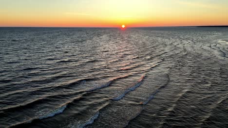 Aerial-view-of-a-sunset-over-a-calm-ocean,-with-streaks-of-orange,-pink,-and-purple-radiating-across-the-sky