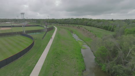 A-drone-view-of-an-adult-male-bike-riding-on-the-Bay-Area-Hike-and-Bike-Trail-behind-Clear-Lake-High-School-on-an-overcast-day-in-Clear-Lake,-Houston,-Texas