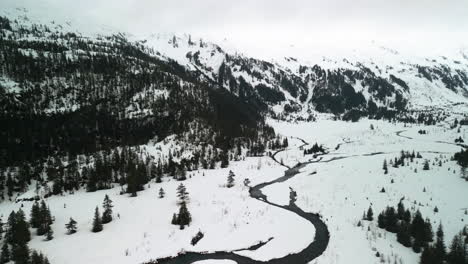 Drone-tilting-over-a-small-river-in-a-mountainous-landscape-in-snowy-Alaska