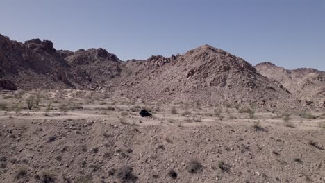 Drone-footage-of-a-black-Land-Rover-Defender-SUV-driving-across-a-desert-landscape